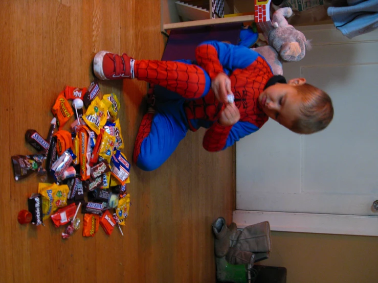 a little boy in a spiderman costume is playing with an assortment of candy