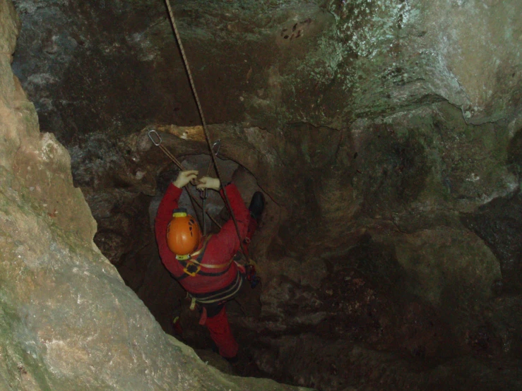 the man is climbing up on a rope inside of the cave