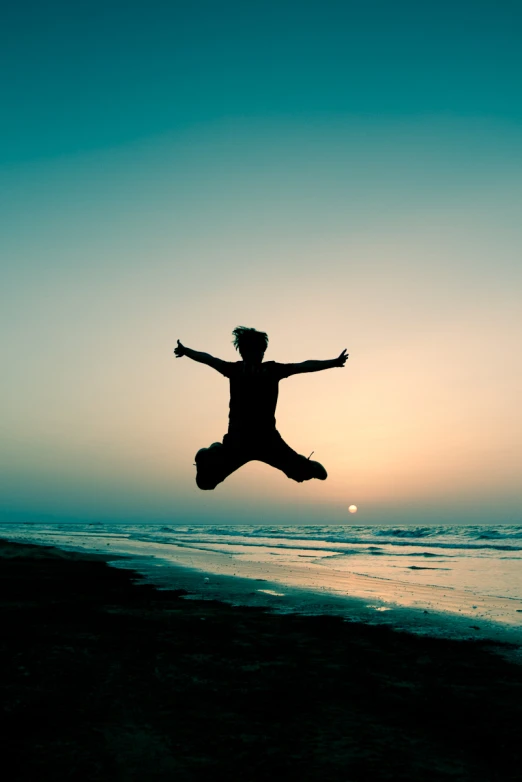 a person jumping in the air on top of a beach
