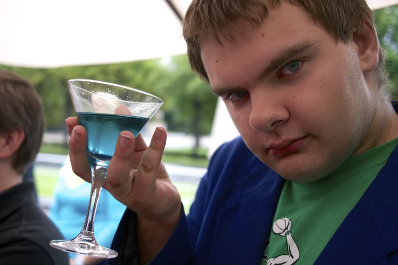 a young man drinking a drink out of a tall martini glass