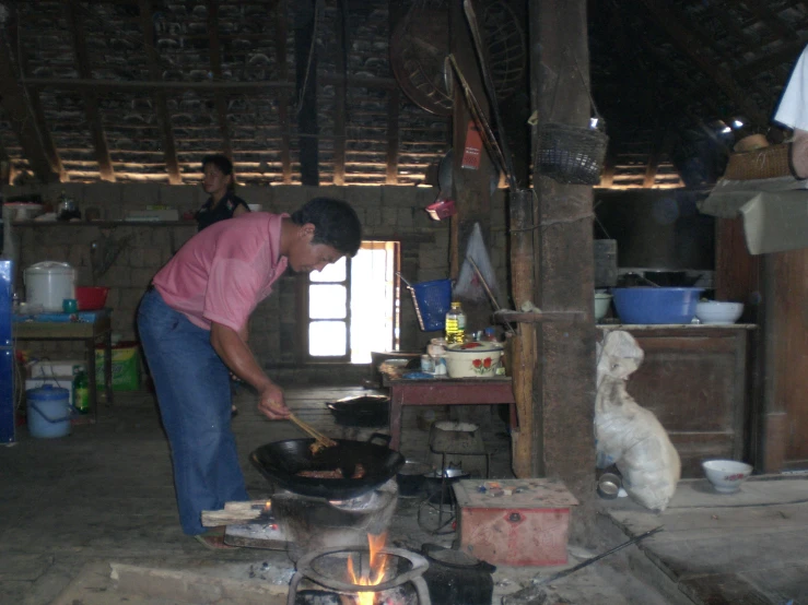 a man preparing food in a hut with a fireplace
