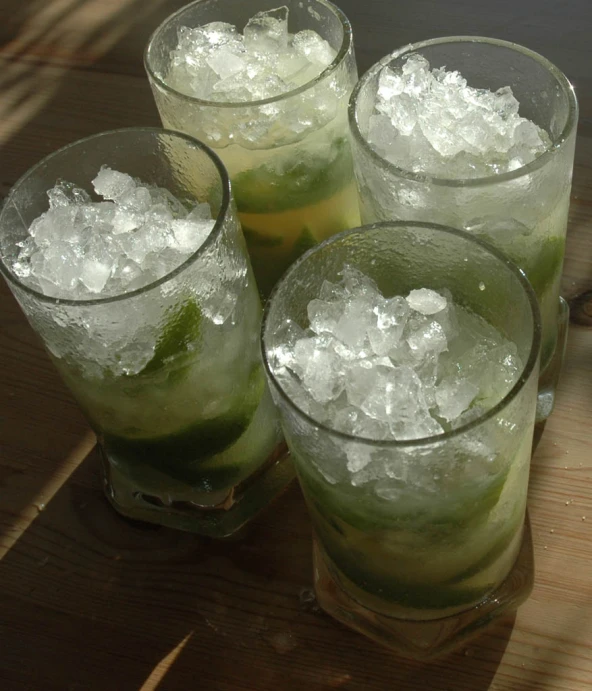 three glasses filled with green liquid next to another glass filled with ice