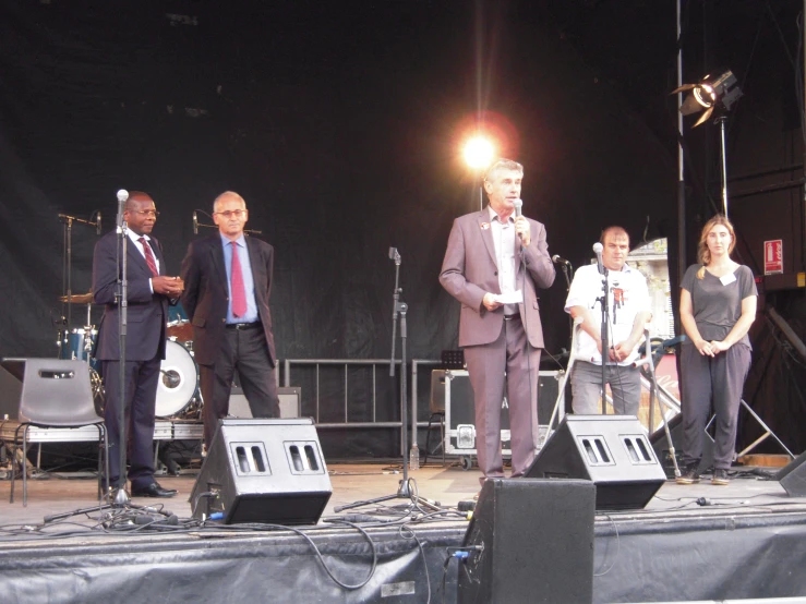 the group of men are on stage, the men in business attire are singing and watching soing