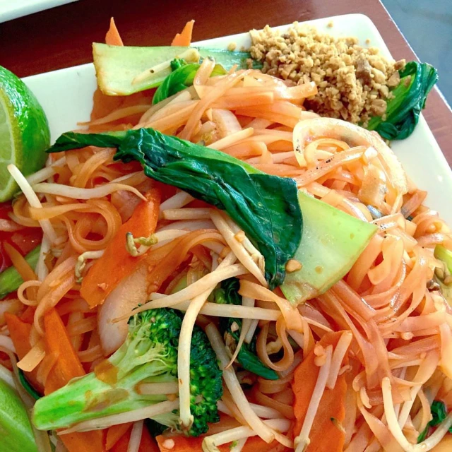 a plate filled with noodle and vegetables sits on a table