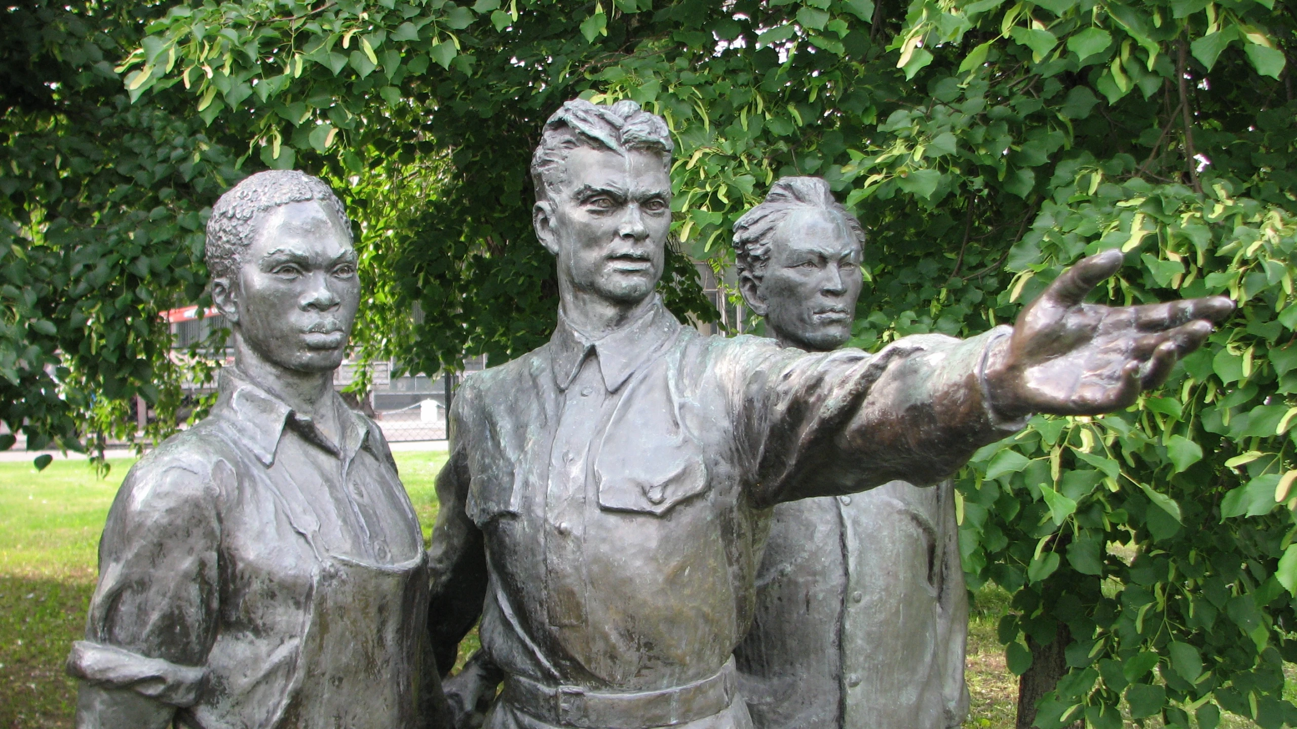 a statue of three people next to some bushes