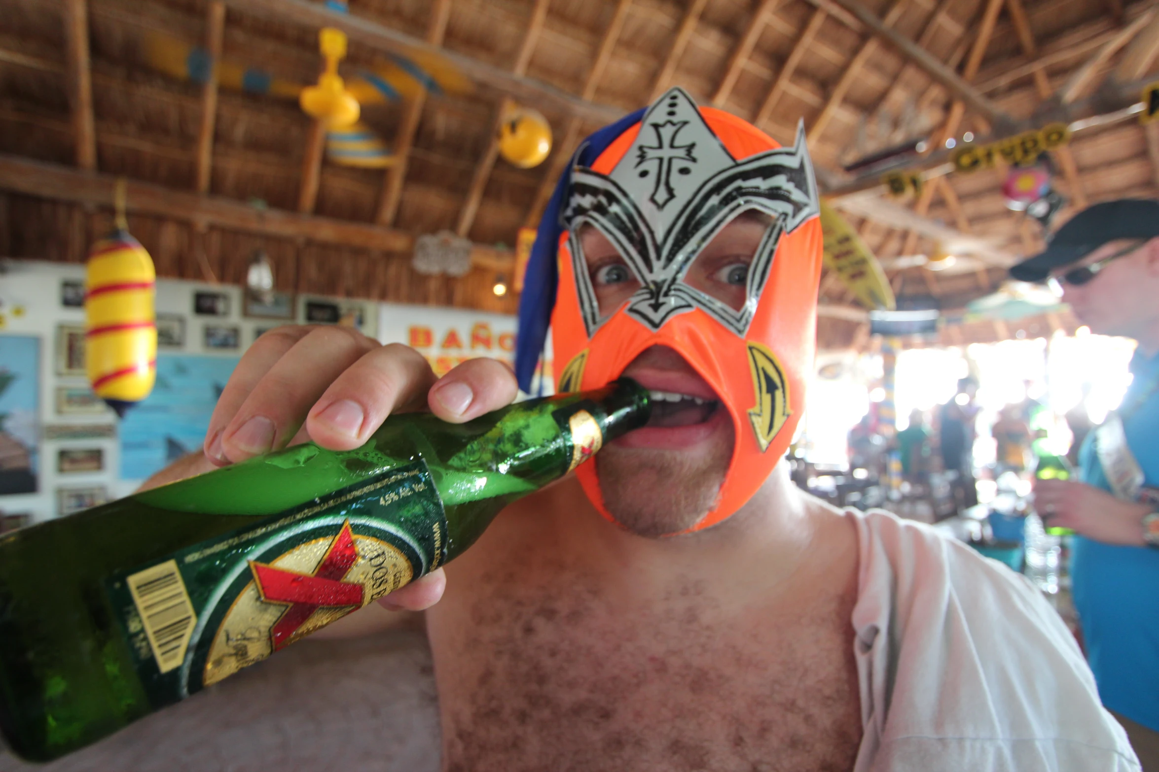 a man wearing a helmet on his head holds a bottle up to the man's face as he opens a beer bottle in his mouth