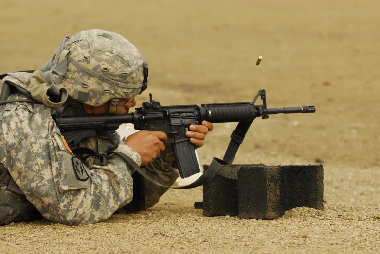 a soldier crouches down and aims at a rifle