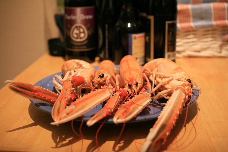 several lobsters with shell and legs lay on a plate on a table next to wine bottles
