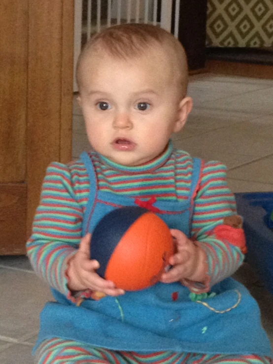 a small child sitting in the floor holding a ball