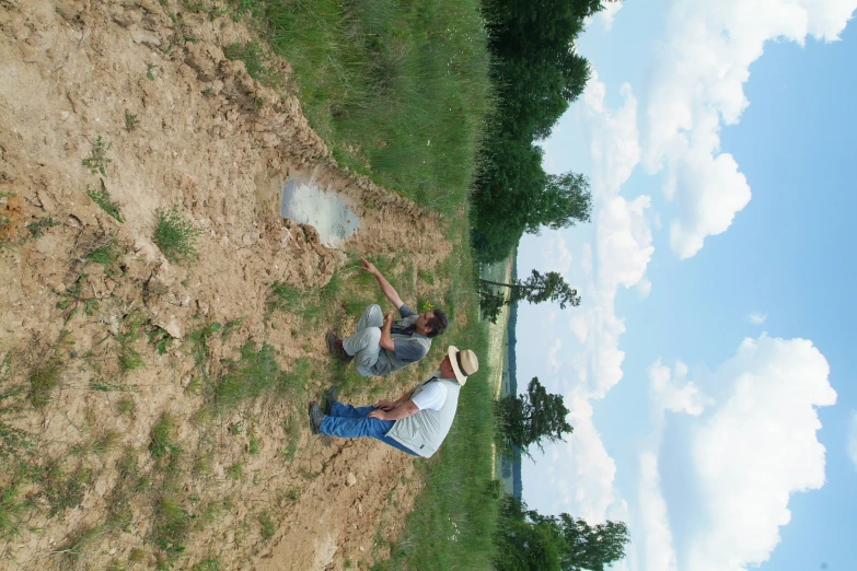 two people digging in a field with a sky background