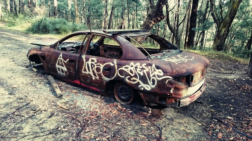 an abandoned car with graffiti on the windows and hood