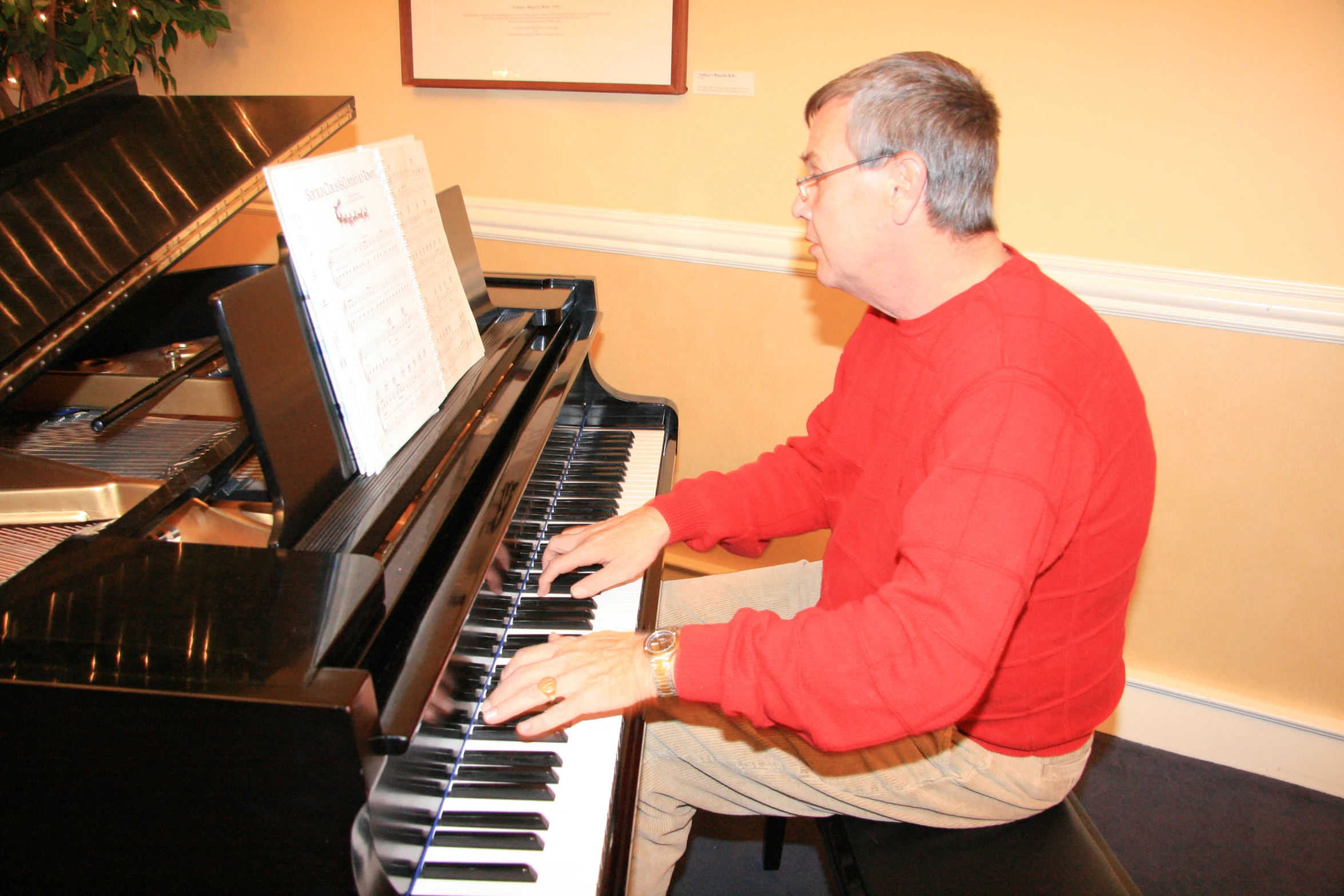 a man in glasses plays an upright piano