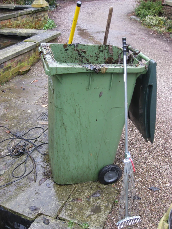 a green trash bin with a yellow plastic handle