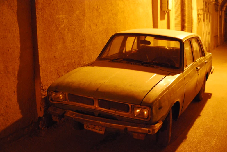 a dirty old car is parked in an alley