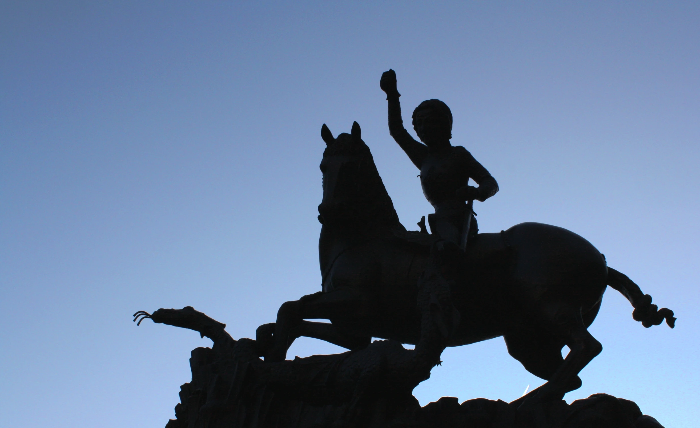 silhouetted statue of man on a horse in front of blue sky