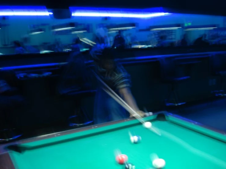 a man in dark outfit playing pool with a green pool table