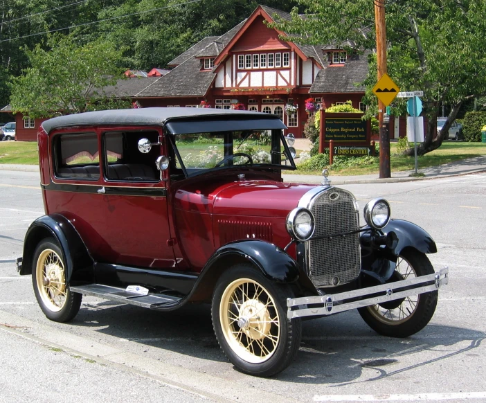 an old model automobile sitting in front of a red house