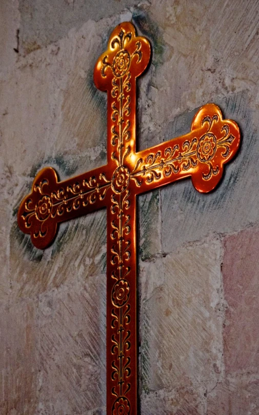 a golden cross sits on the side of a stone wall