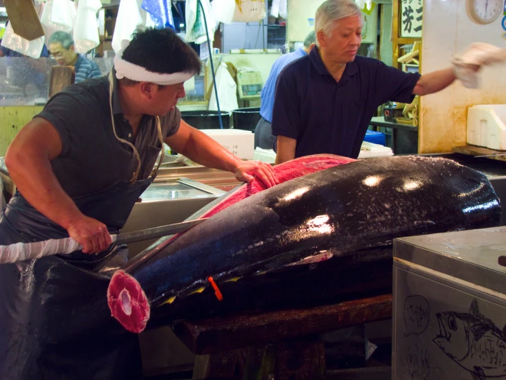 two men are at an assembly line to cut a large fish