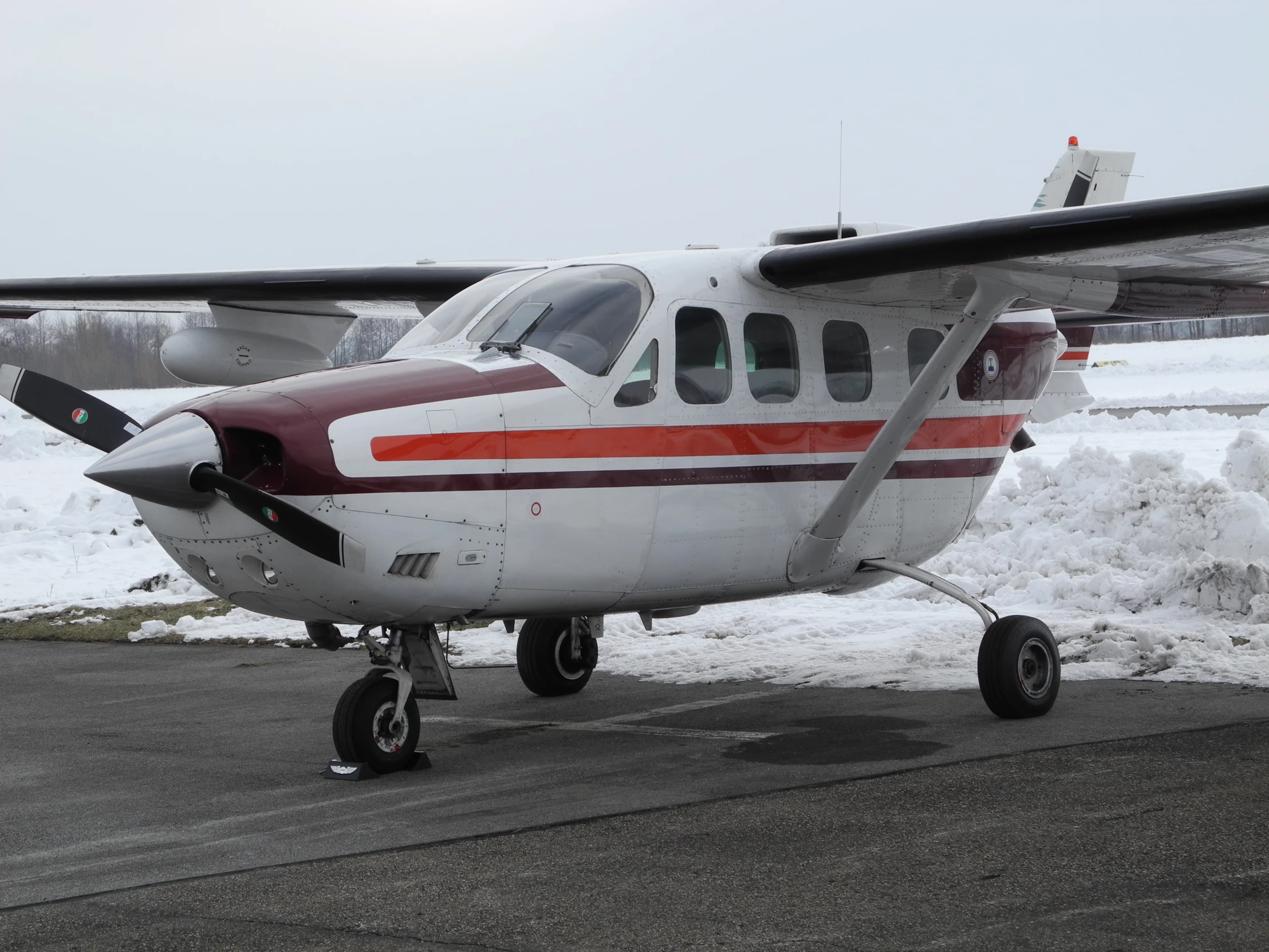 a small red and white plane on tarmac near snow