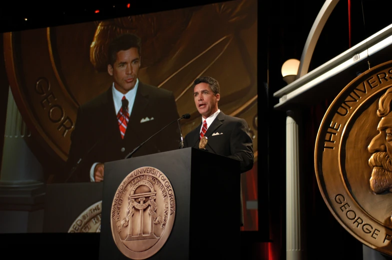 man in business suit standing at the podium on stage while wearing a tie