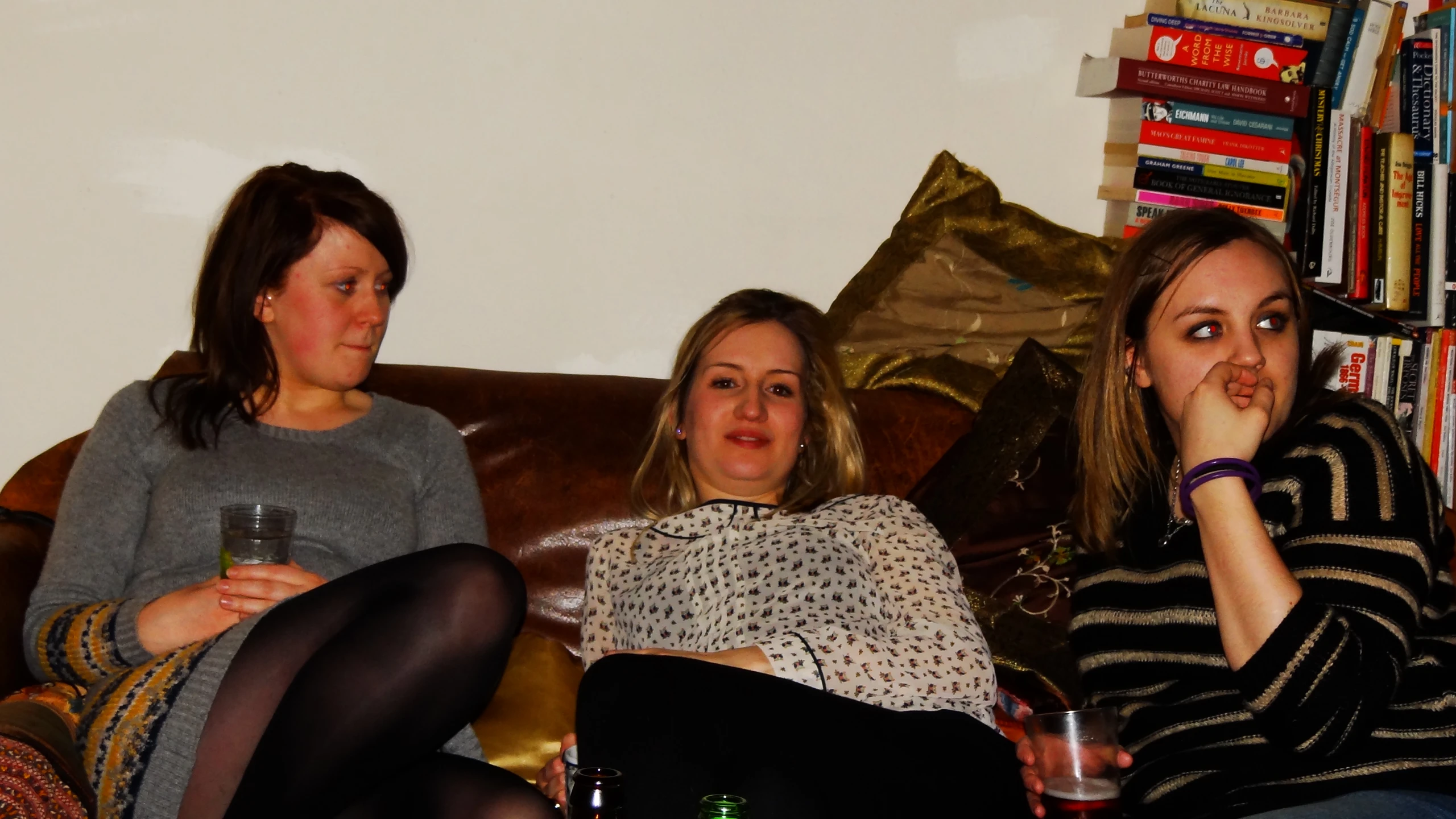 three women are sitting on a couch and drinking a beer