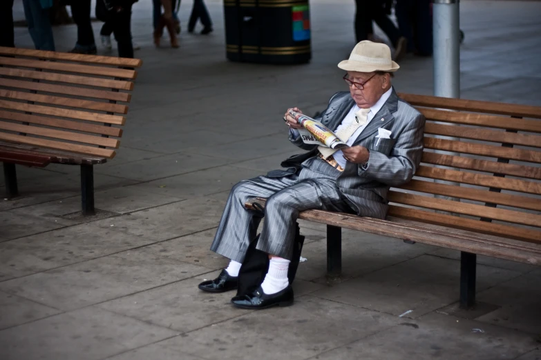 the elderly man sitting on the bench reads