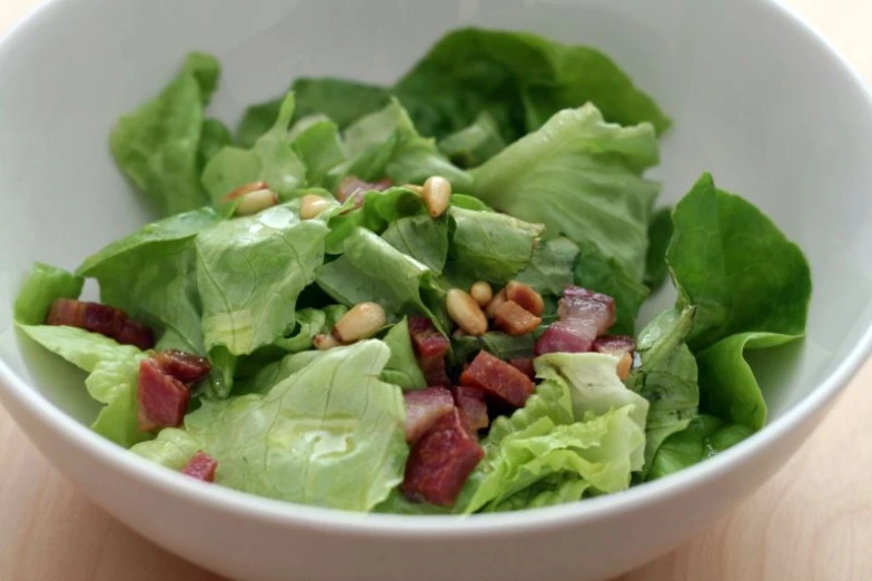 a salad with meat, lettuce and pine nuts in a bowl