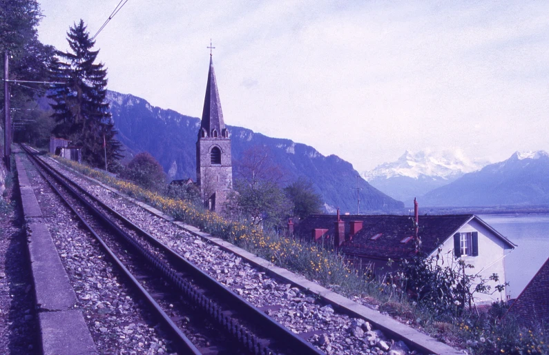 an old church next to a river with mountains in the background