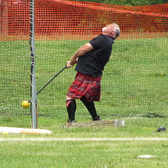 a man in a black shirt and red tartan skirt swinging his stick