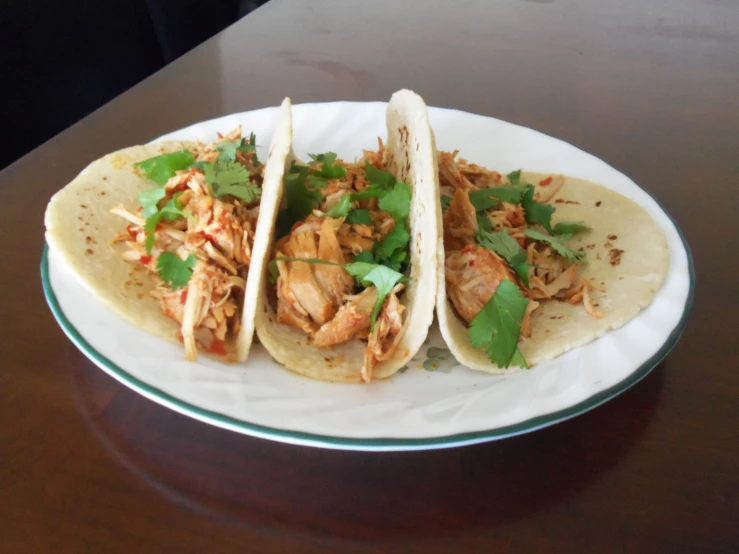 a white plate holding three tacos on top of a wooden table