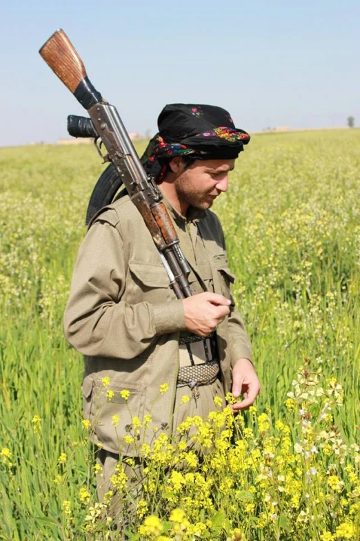 a man in field with rifle and hat walking away from camera