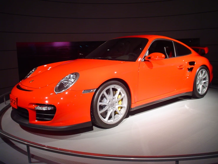 a bright orange sports car on display at an auto show