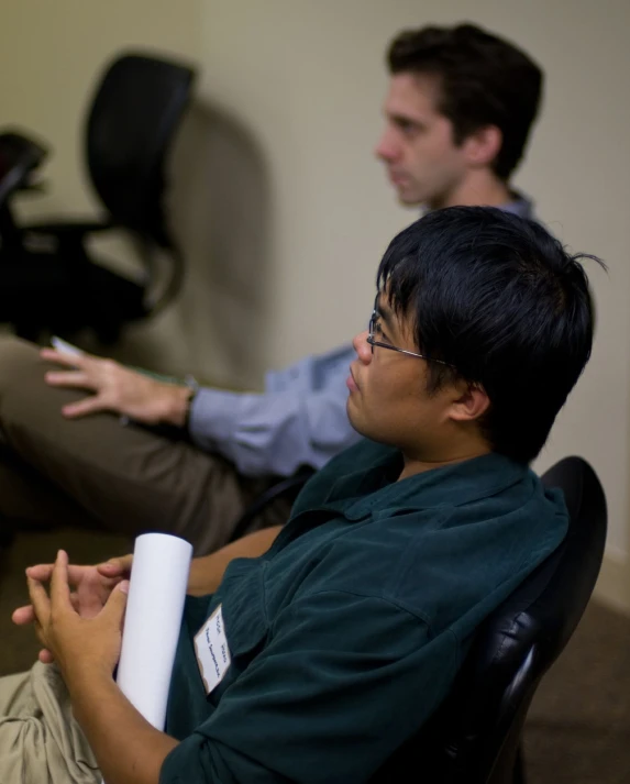 two men sitting in chairs one holding remote