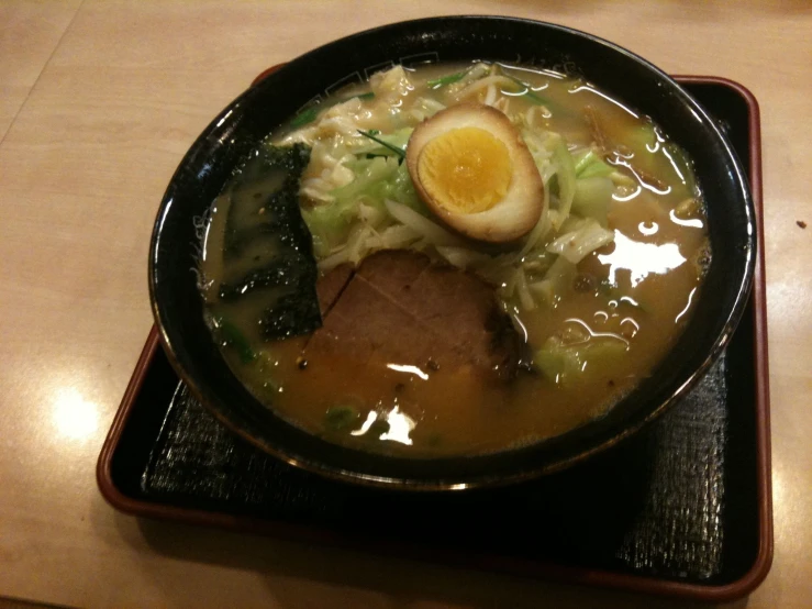 a black bowl containing noodles, meat and egg