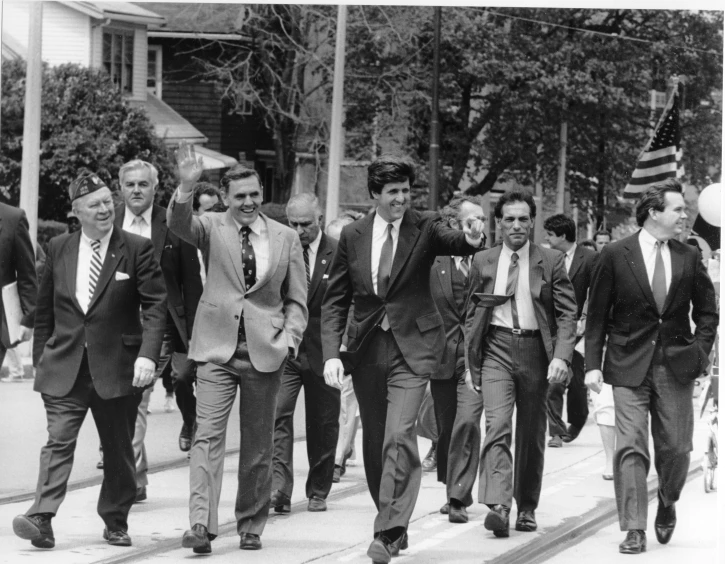 many young men walk down a city street with american flags behind them