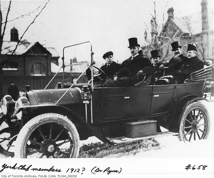a group of men wearing top hats sit in an old car
