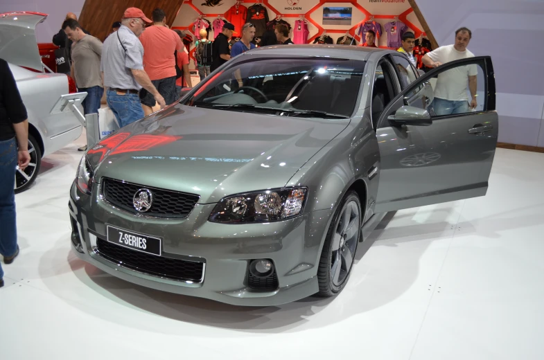 a grey car sitting on top of a floor near a crowd of people