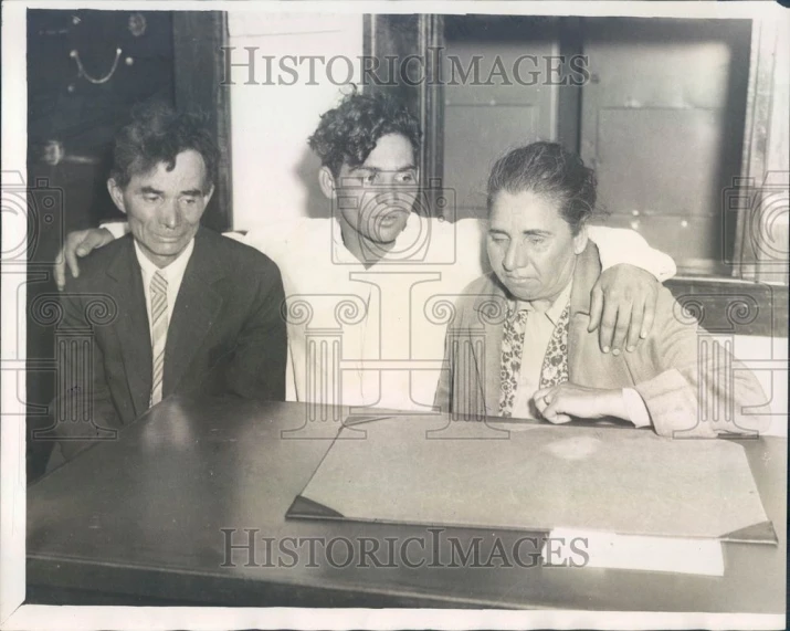 a man with his arm around another mans neck while sitting at a table