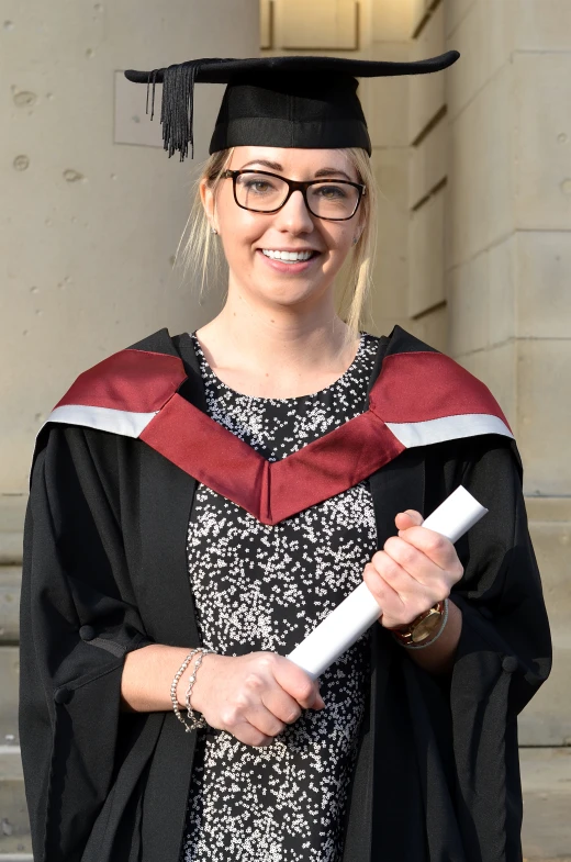 a woman wearing a red and black gown and cap holding a white sheet