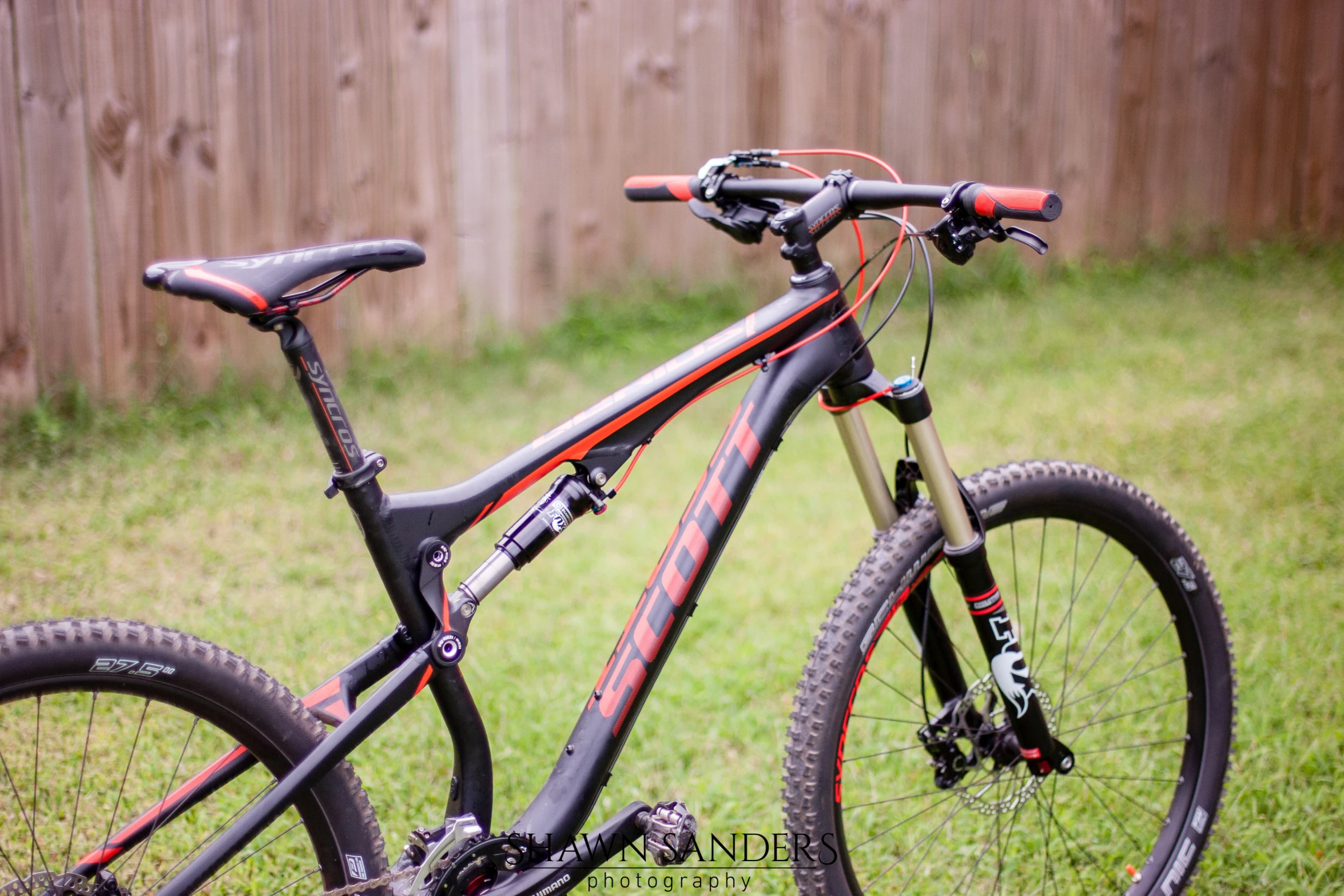 the bicycle is standing in the grass next to a fence