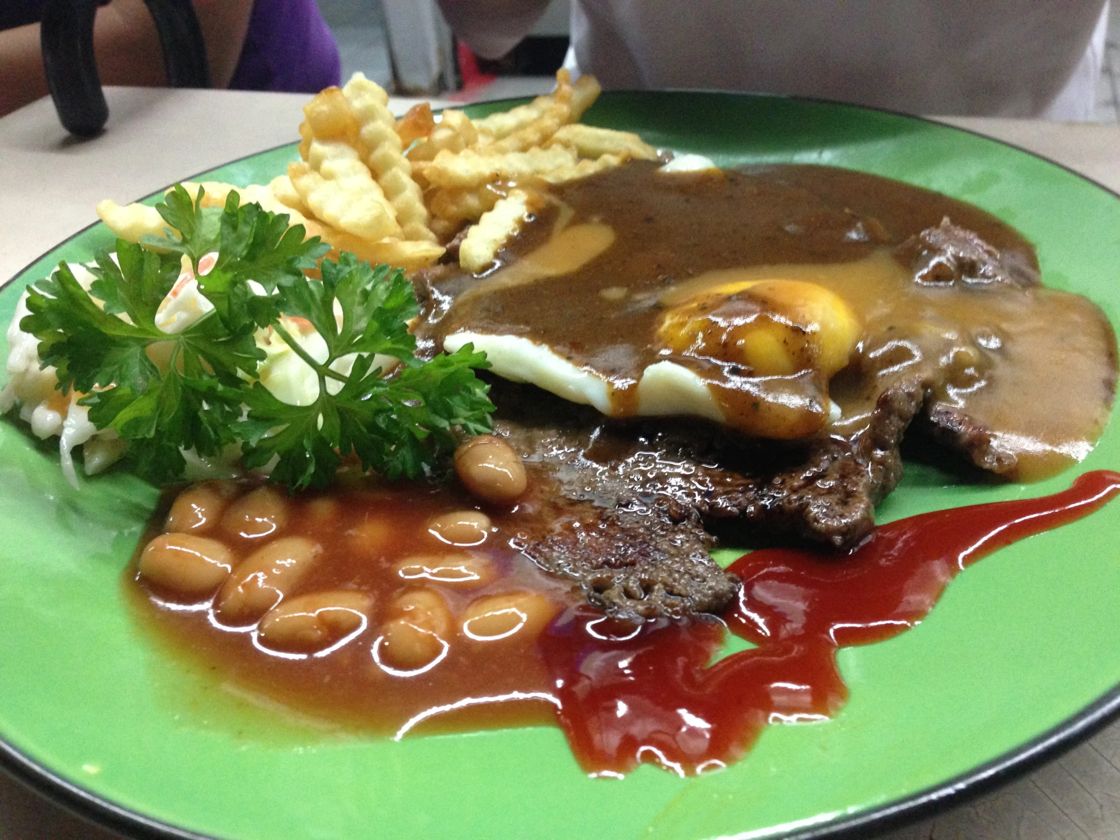 the green plate has a sandwich, baked potatoes and greens on it