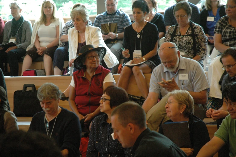 people sit in a crowd next to one another while another holds a piece of paper