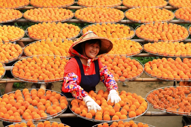 a smiling woman wearing a hat with many shelves full of oranges