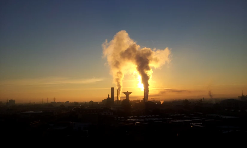 a factory emits steam from its chimney at sunset