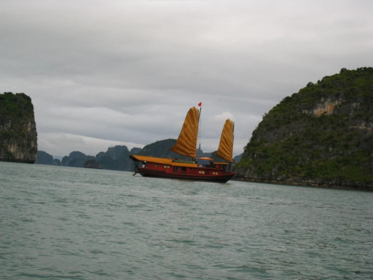 an orange ship with sails floating by a mountain