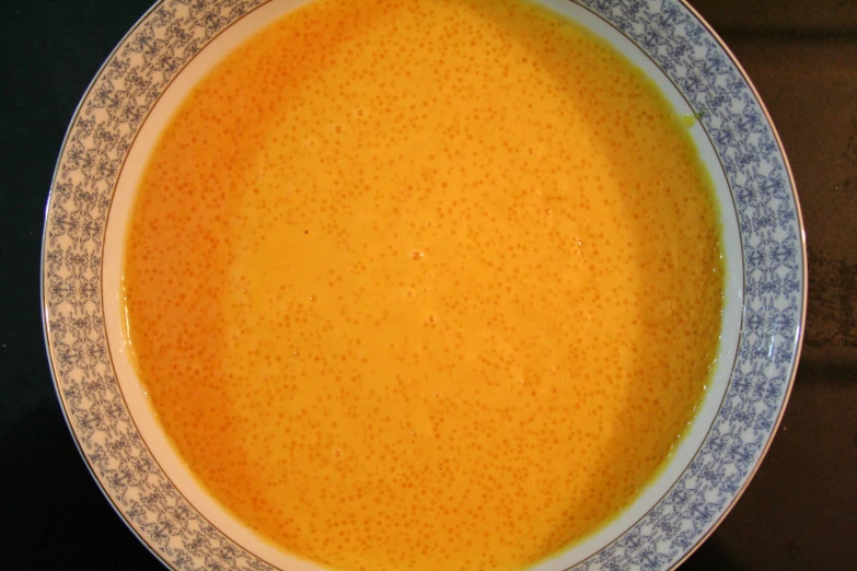 a bowl of yellow soup that has an elaborate rim