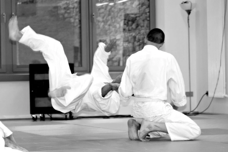 two people in white clothing, one on his back and the other upside down