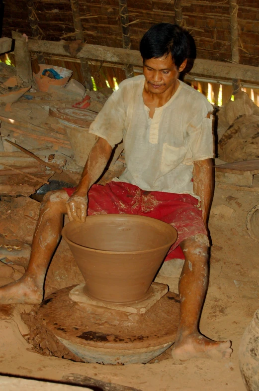 a man sitting on a pottery wheel throwing a pot on it