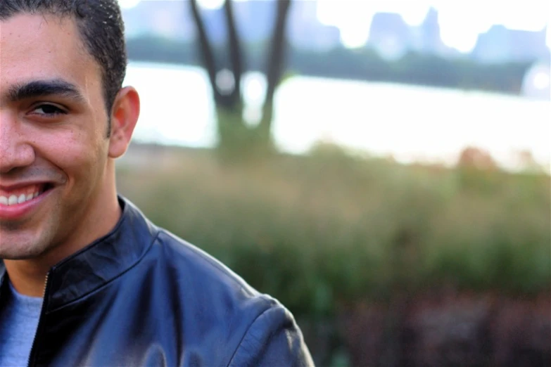 a man smiling with a black jacket and green shirt on